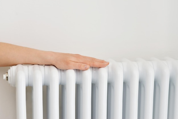 Girl warms up the frozen hands above hot radiator close up view