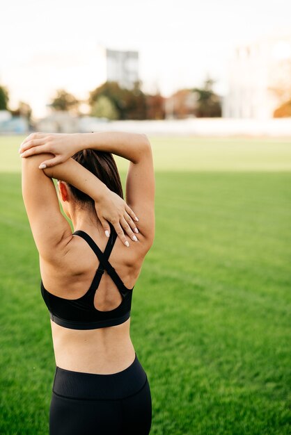 The girl warms up the upper body in the stadium in the morning