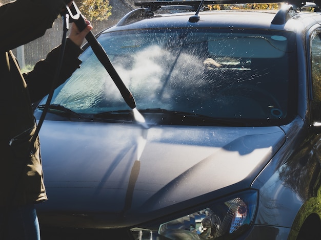 The girl washes the car at home near the garage using a pressure washer