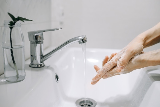 Girl washes her hands thoroughly with soap under water in a white bathroom side view Conceptual photo of cleanliness