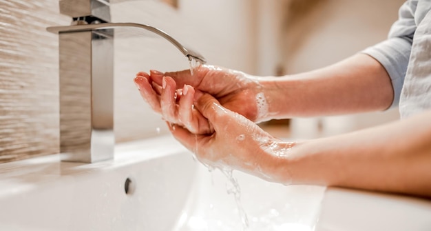 Foto ragazza che si lava le mani con schiuma di sapone in bagno con igiene del rubinetto in acciaio e procedura di pulizia