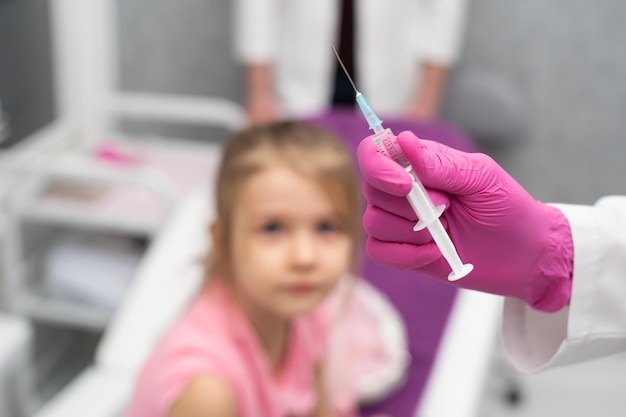 The girl watches curiously as the doctor prepares the syringe for injection Preventive vaccine for young children