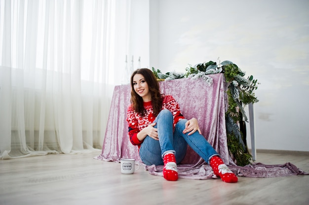 Girl wear on winter sweater sitting against table at room with chrismas decorations.