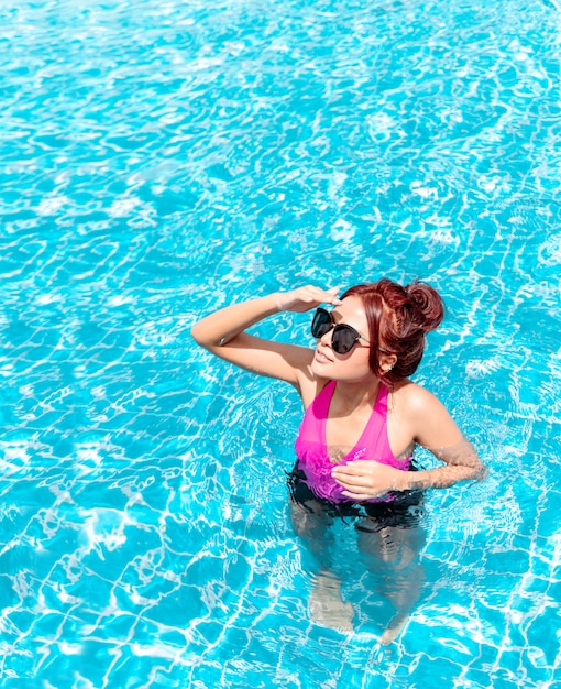 Photo girl wearing bikini or swimwear are sunbathing by the pool.