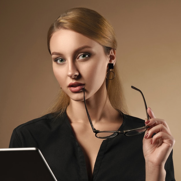 Girl wearing black shirt taking off eye glasses while using tablet on beige background