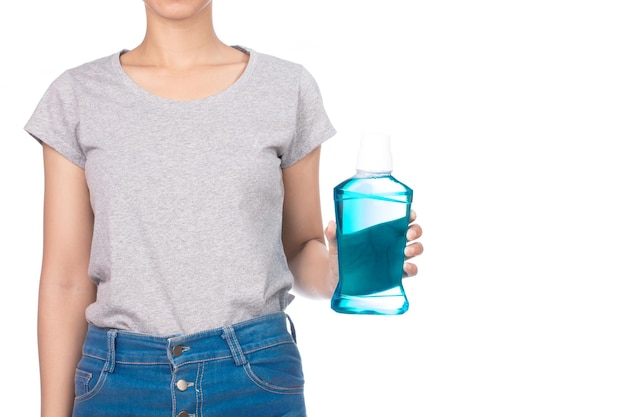 girl wearing blank gray t-shirt, jeans holds a mouthwash bottle isolated on white background.