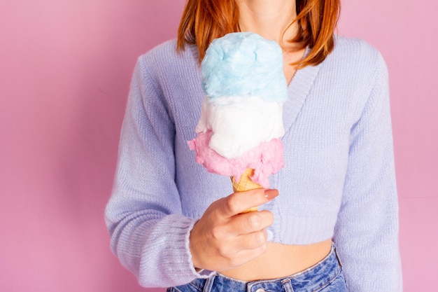 青いセーターとジーンズを着て、綿菓子のアイスクリームを持っている女の子。淡いピンクの背景。
