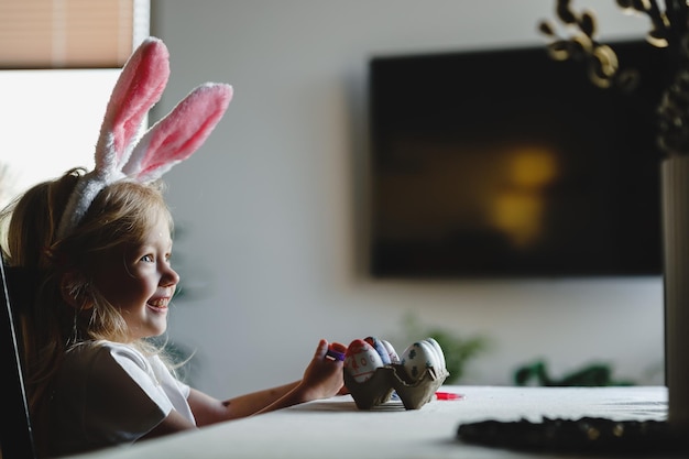 Photo a girl wearing bunny ears sits at a table in front of a tv.