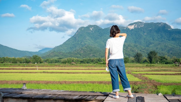 木製の通路にカジュアルなシャツを着た女の子が自然の山々の田んぼの新鮮な空気を見る