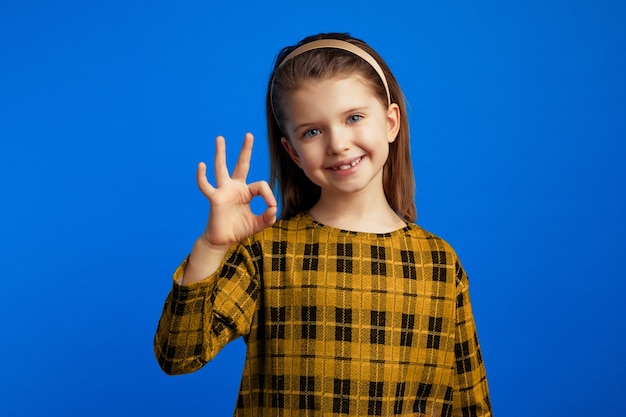 Girl wearing checkered dress looking at camera and showing okay sign