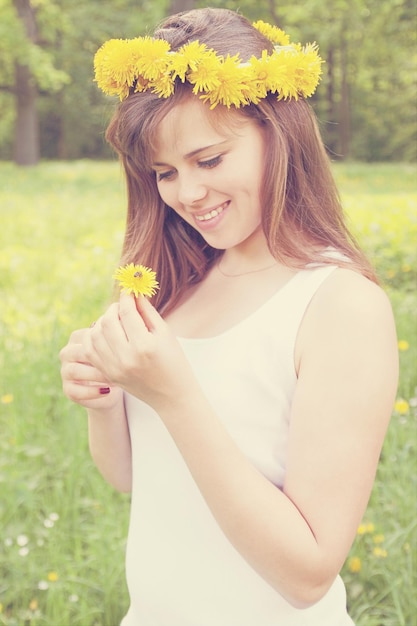 A girl wearing a crown holding a dandelion to a bee