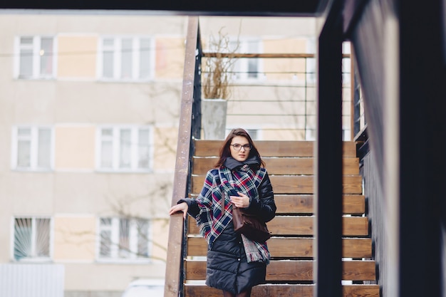 A girl wearing eyeglasses in winter wears wooden stairs