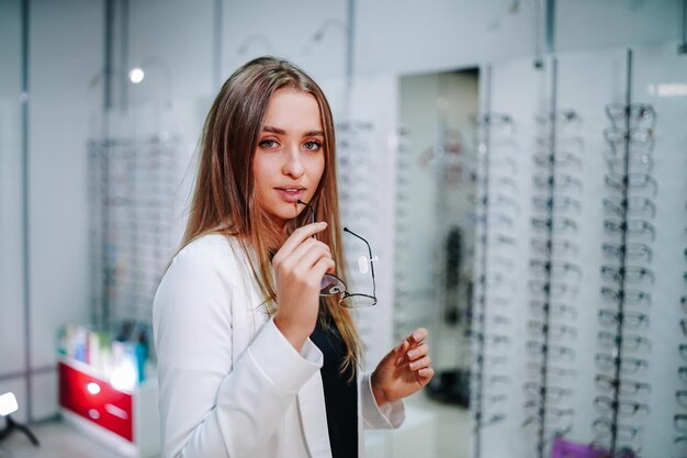 Girl wearing glasses Happy female optometrist optician is standing with set of glasses in background in optical shop Stand with spectacles and eyesight correction concept