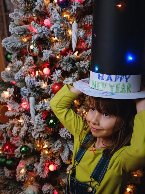 Photo girl wearing hat while standing by christmas tree at home