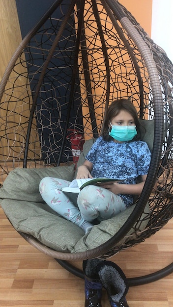 Photo girl wearing mask holding book sitting on swing