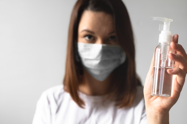 Girl wearing a protective medical mask holding a bottle with a sanitizer. Protect your health
