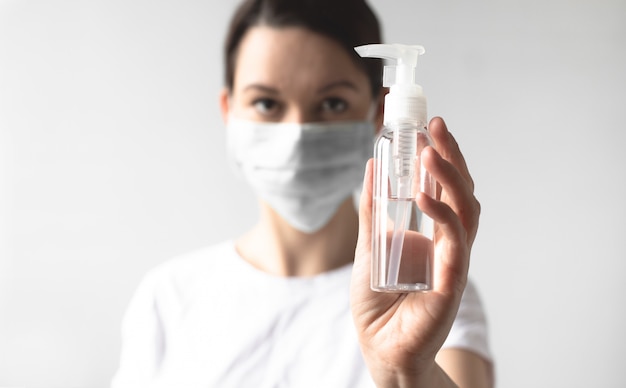 Girl wearing a protective medical mask holding a bottle with a sanitizer. Protect your health