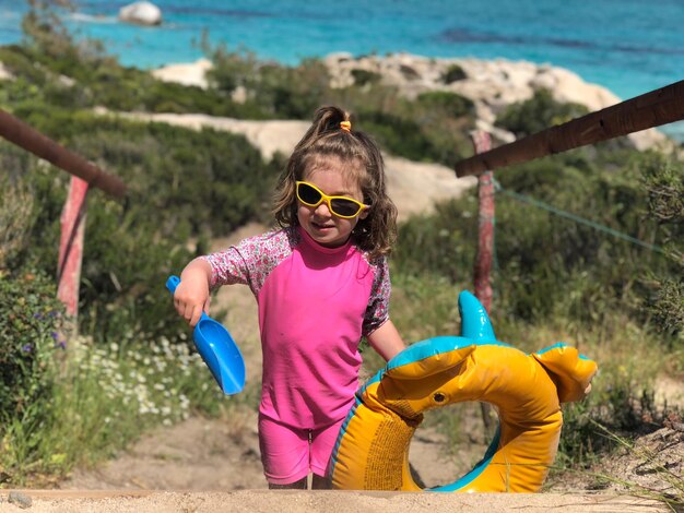 Photo girl wearing sunglasses while holding inflatable ring and toy at beach