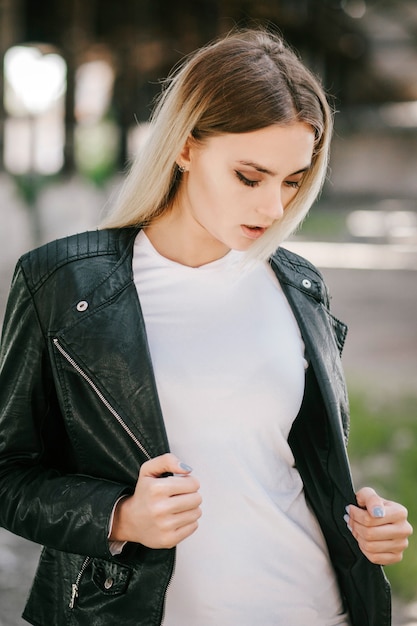 Girl wearing t-shirt and leather jacket posing against street