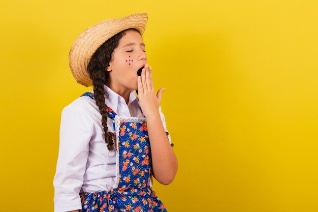 フェスタジュニーナの典型的な服を着た女の子が眠い感じであくびをする口を手渡しますフェスティバルのためにアライアを行います