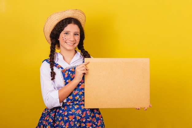 Girl wearing typical clothes for Festa Junina holding screen for text or ad For the Arraia party