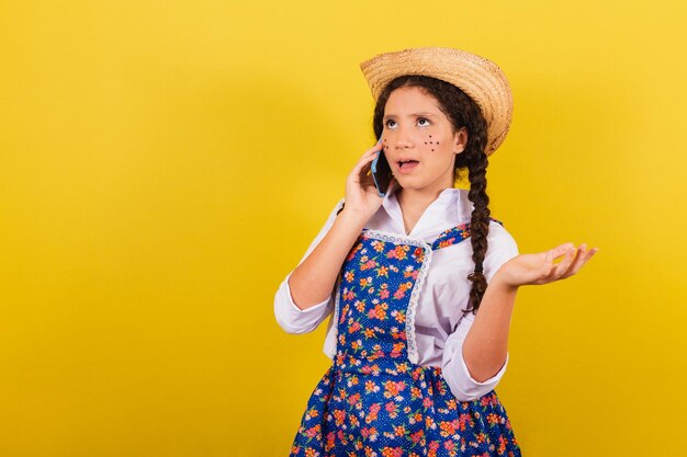 Girl wearing typical clothes for festa junina on mobile voice\
call connected call for the arraia party