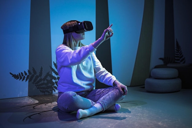girl wearing virtual reality glasses in the blue lighted room making hands and finger moves in the