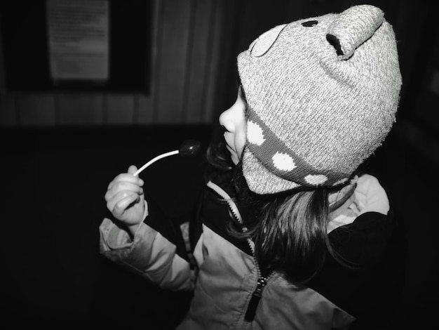 Girl wearing warm clothing eating lollipop at night