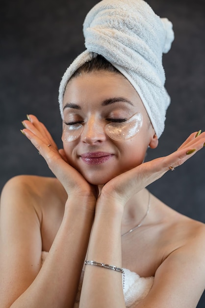 Girl wearing white towel use eye patches for puffiness wrinkles isolated on black