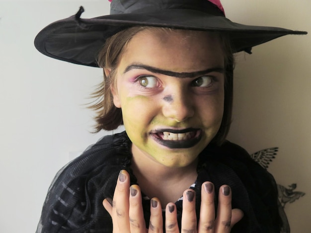 写真 魔女の衣装と帽子を着た女の子がハロウィーンで壁に立って歯を締めている