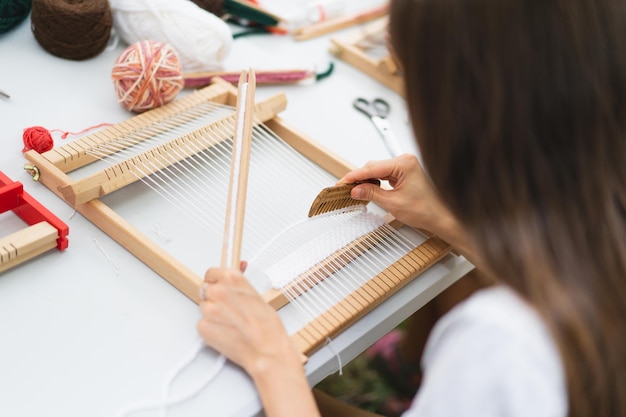 Foto ragazza che tesse un piccolo tappeto con motivo alla masterclass sulla tessitura la ragazza sta studiando come tessere su un telaio manuale da tavolo processo di creazione concetto fatto a mano