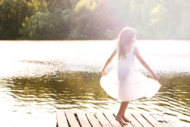 A girl in a wet white dress dancing on the river pier