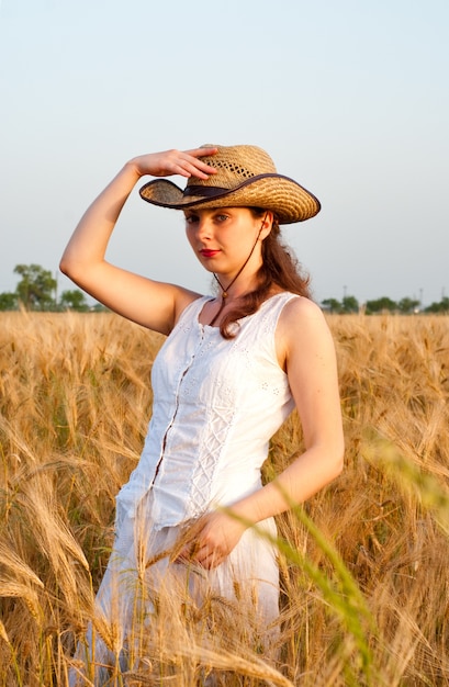 Girl in wheat field in white dress and stetson hat. Selective focus.