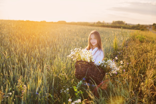 Girl in the wheat field with basket of flowers