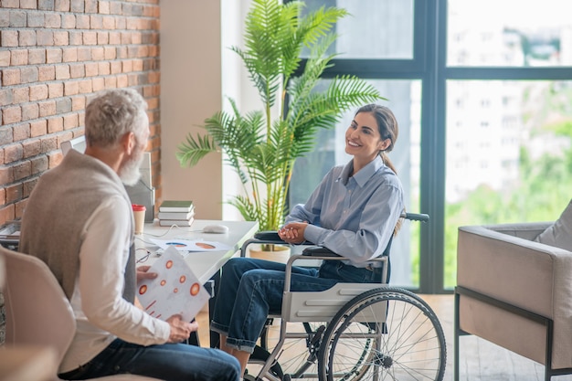 A girl on a wheelchair talking to her male colleague and looking involved