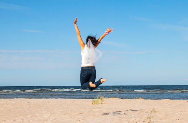 Girl in a white blouse jumps to the sky on the shore of the blue sea