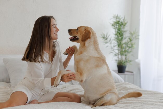 Girl in white clothes with dog labrador playing at home