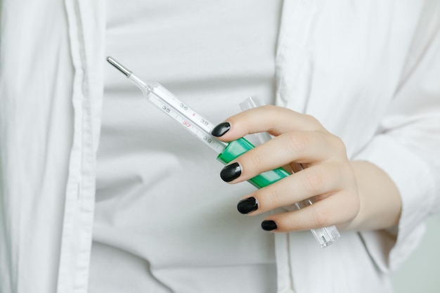 A girl in a white coat holds a thermometer to measure body\
temperature a medical worker a nurse h