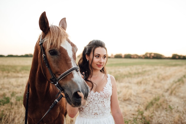 Girl in a white dress next to a brown horse in the village