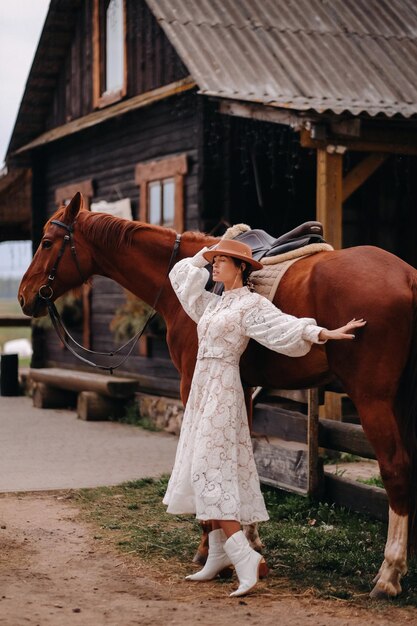 A girl in a white dress and a hat is standing next to a horse