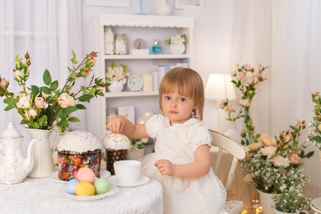 A girl in a white dress is sitting at a table and watching Easter holiday