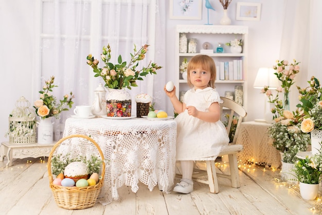 A girl in a white dress is sitting at a table and watching Easter holiday