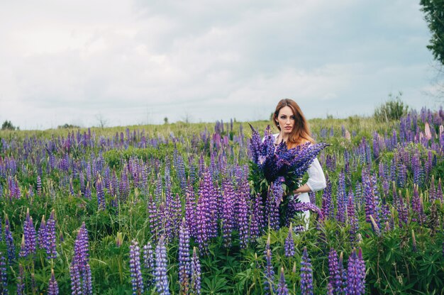 A girl in a white dress is standing among the lupines