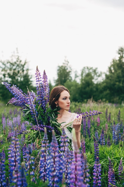 A girl in a white dress is standing among the lupines