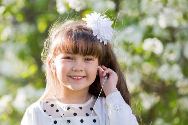 A girl in a white dress listens to music through small audio headphones.