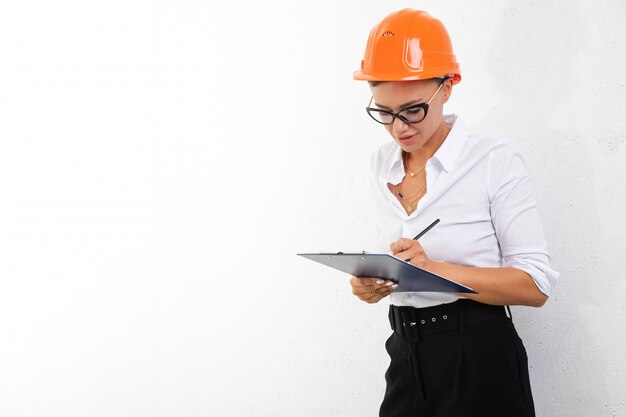 Girl in a white dress shirt with orange construction helmet signs documents on white