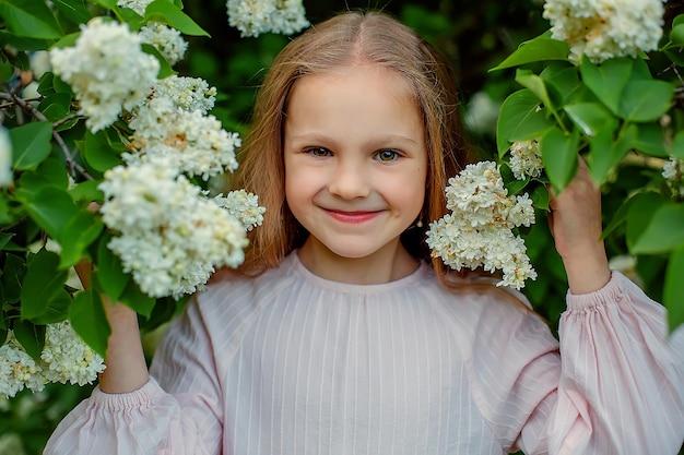 A girl in a white dress smiles in front of a bush of white flowers