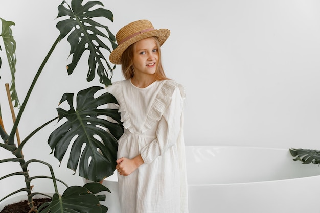 девушка в белом платье и соломенной шляпе в комнате с растениями и ванной