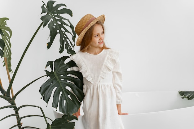 a girl in a white dress and a straw hat in a room with plants and a bathroom