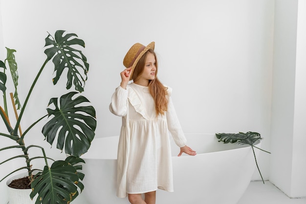 a girl in a white dress and a straw hat in a room with plants and a bathroom